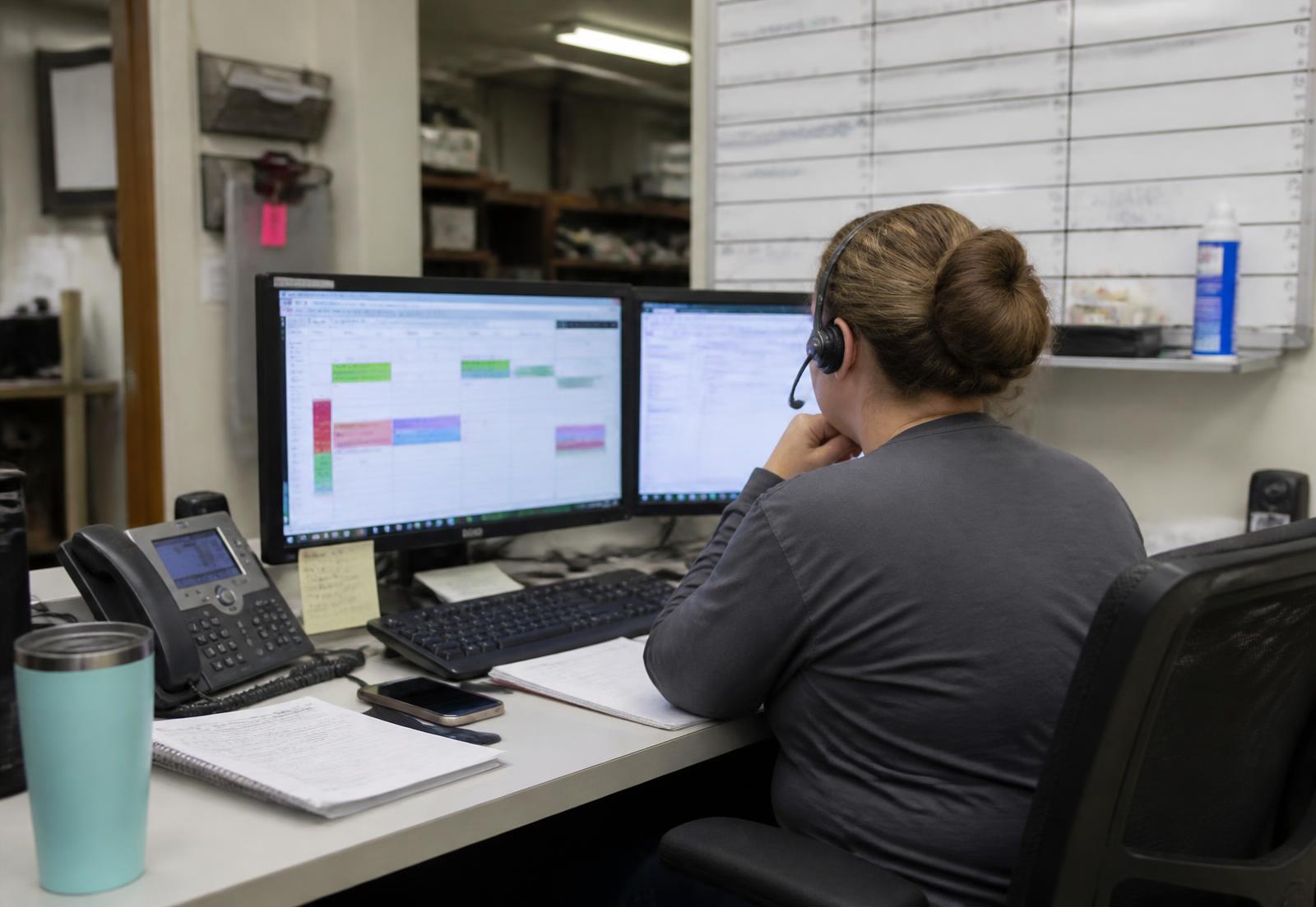 Dispatcher at a service company desk working a scheduling board with a headset on